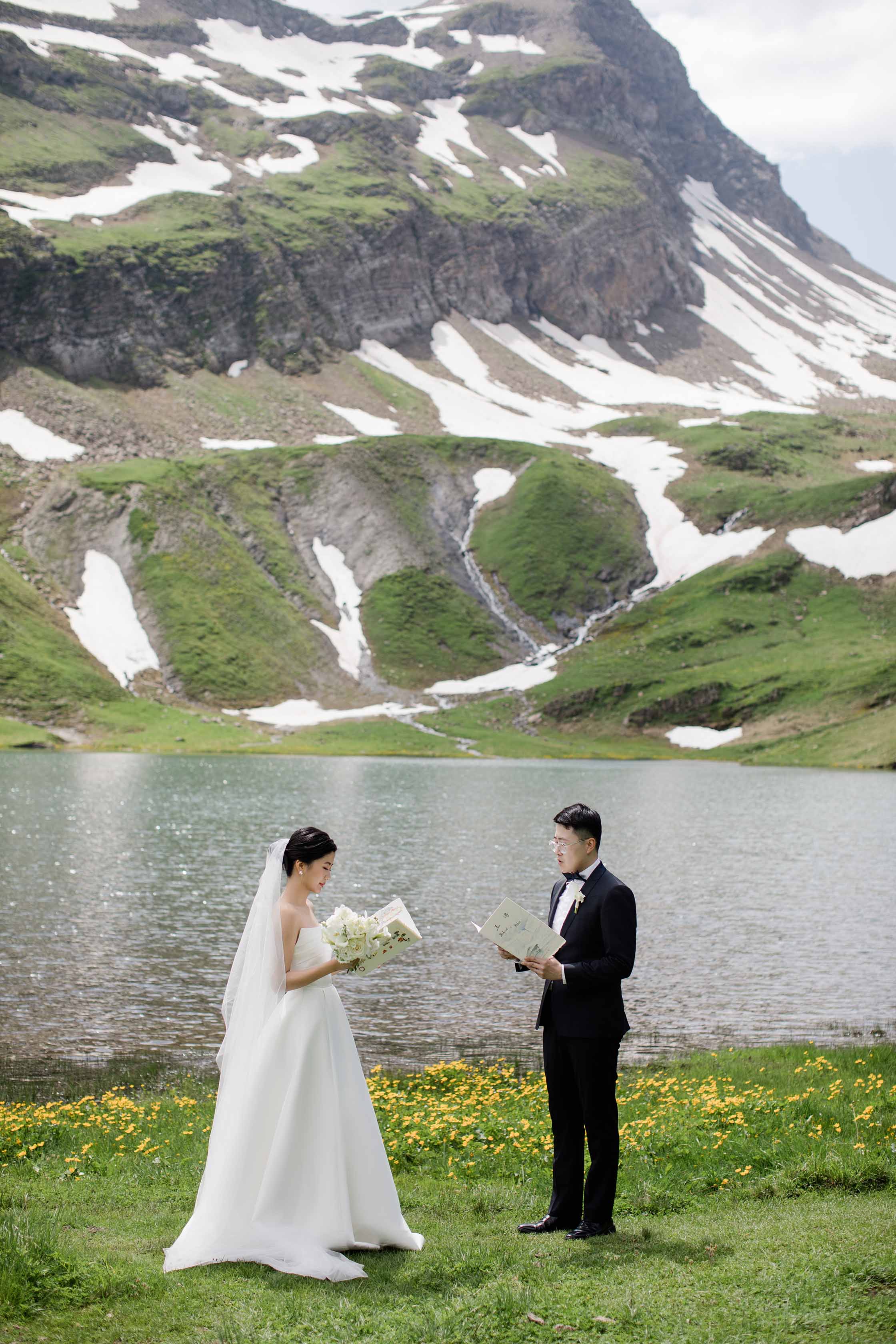 Prewedding & Elopement in Switzerland image of a couple in a mountain landscape with a lake, groom reading to bride.