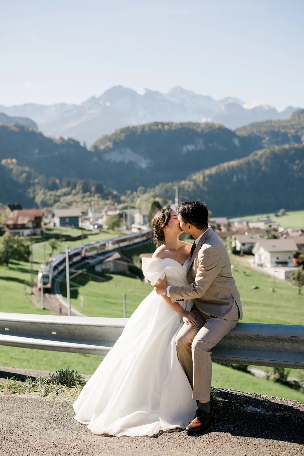 Authentic destination wedding moment with a couple in love and the iconic Swiss red train winding through the Grindelwald valley below.