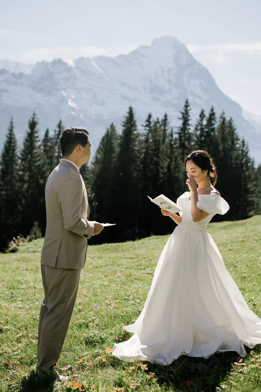 Intimate wedding ceremony in Grindelwald First with the bride gently wiping a tear while reading handwritten vows during golden hour lighting.