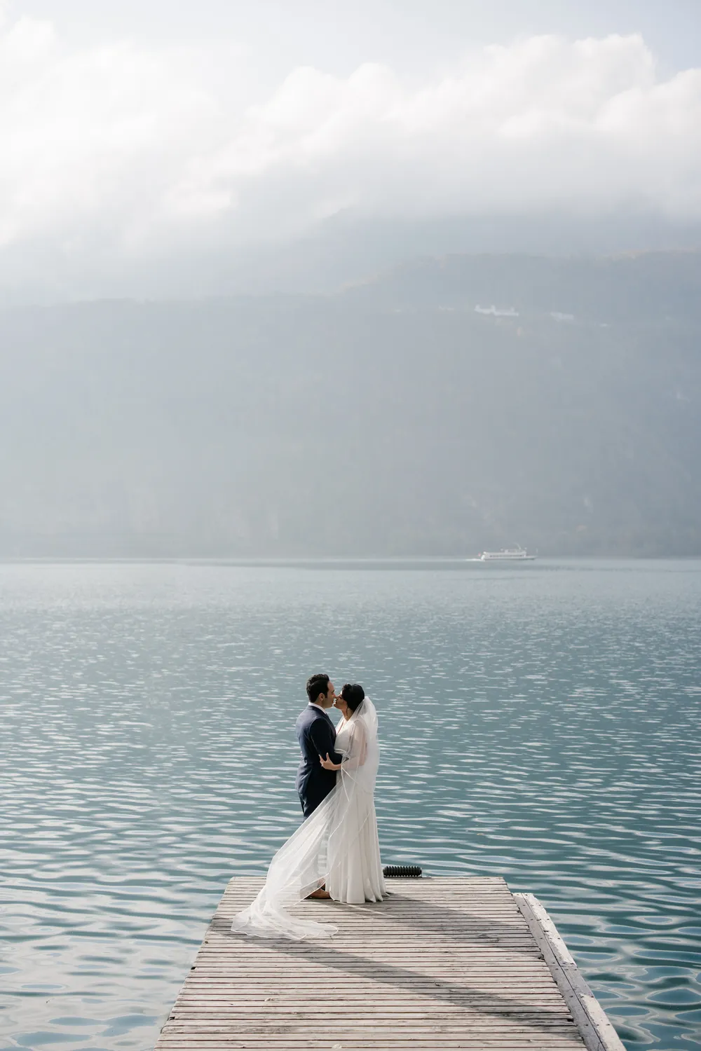Cinematic pre-wedding portrait on a wooden pier at Walensee, Switzerland, during a misty November morning.