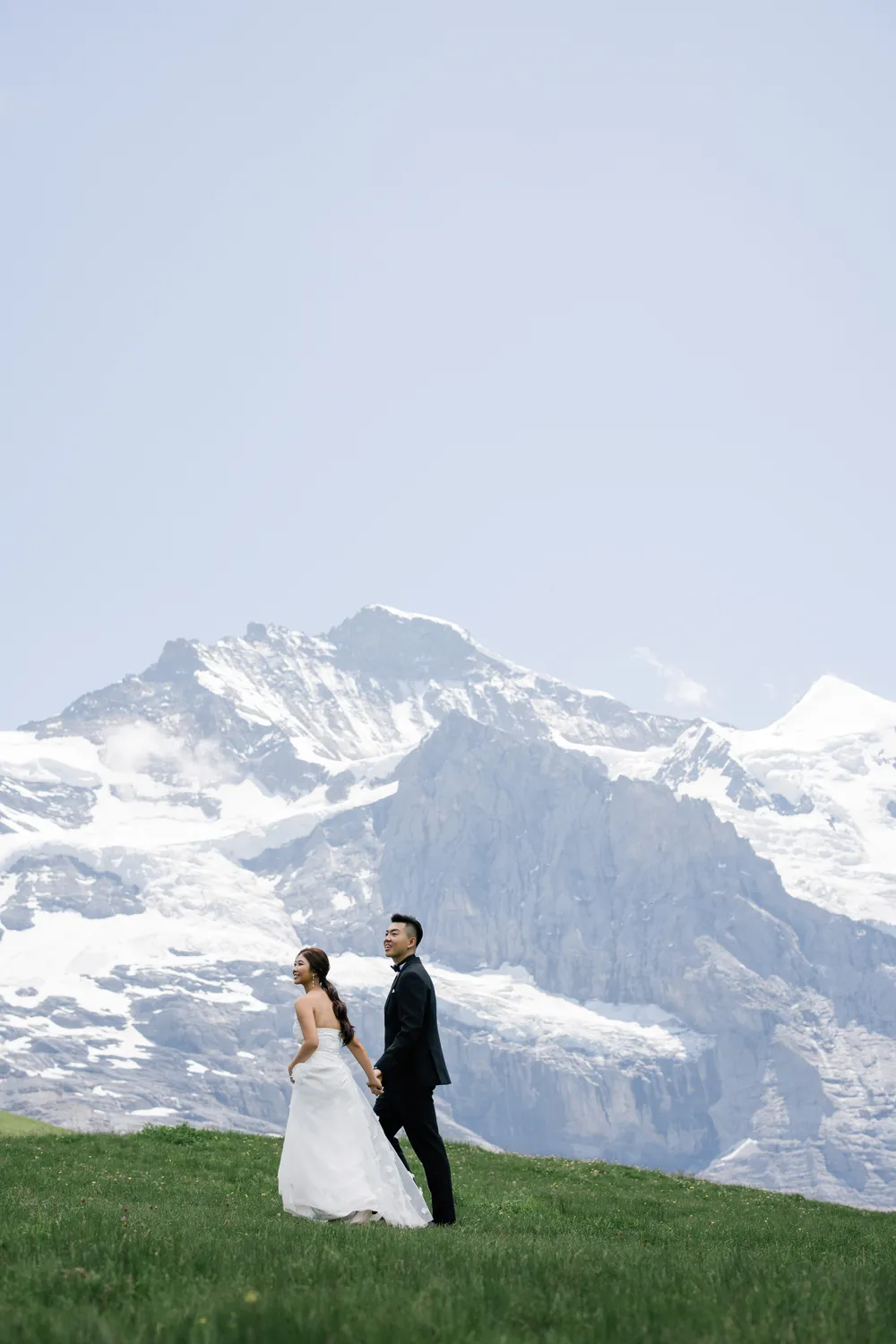 Intimate pre-wedding portrait with the massive snow-capped Jungfrau peaks background at **Kleine Scheidegg** in **June**.