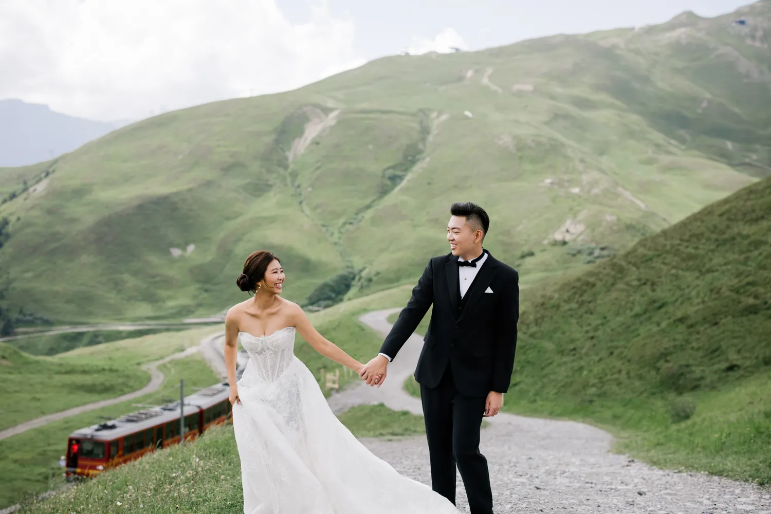 Bespoke pre-wedding portrait on a mountain ridge at **Kleine Scheidegg**, overlooking the Eiger Express and distant Swiss lakes.