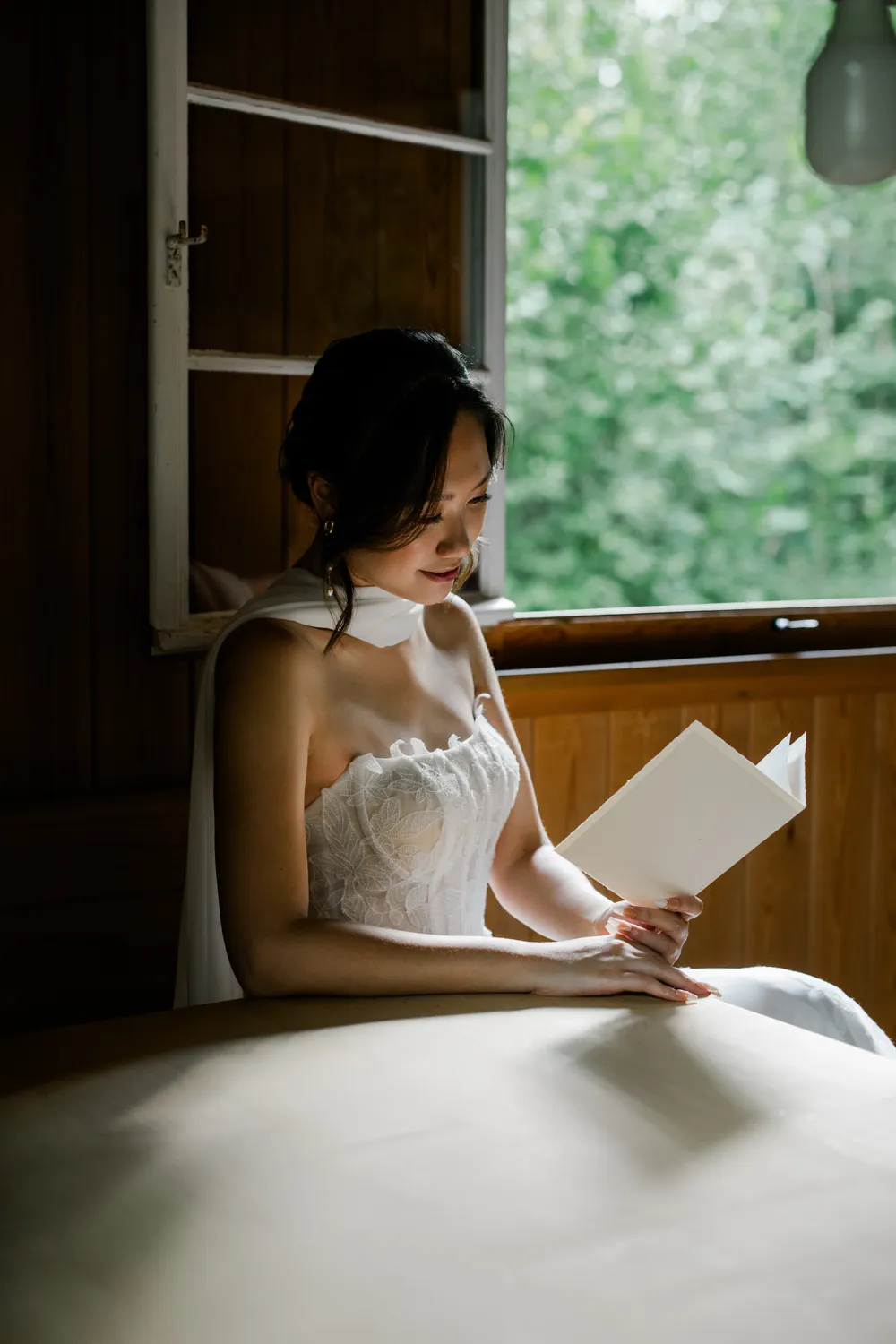 Soft window light illuminating a bride reading her vows in a rustic Swiss cabin